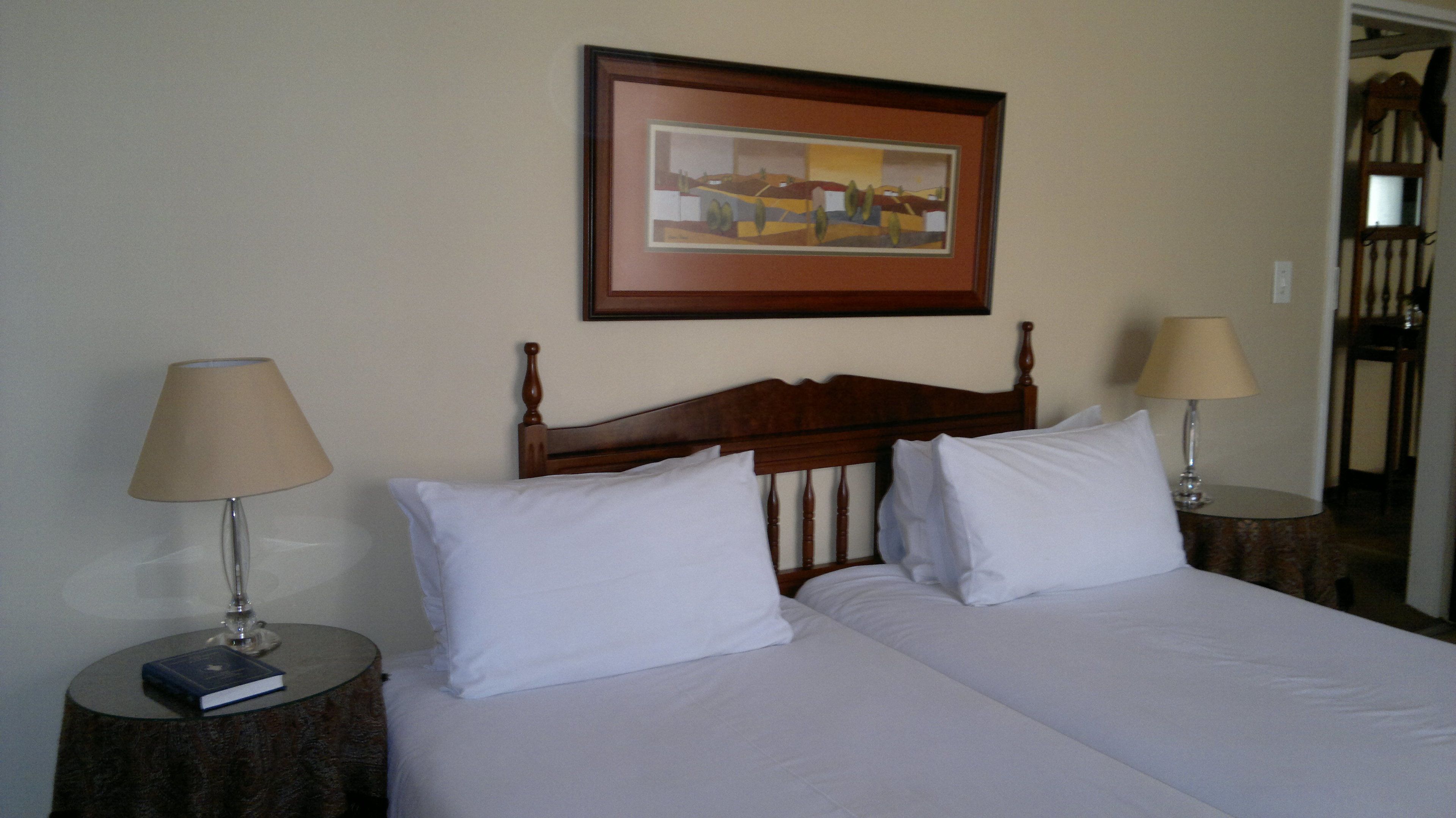 A double bed with white linens, two bedside tables with lamps, and a framed picture on the wall.
