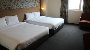 Ein Hotelzimmer mit zwei Betten, einem Holz-Kopfteil, einem Fenster mit Vorhängen und einem Sessel.