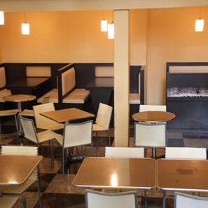 A restaurant interior with booths and tables, pendant lighting, and a wall-mounted menu display. - Strand Hotel (Singapore)