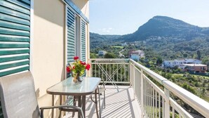 En balkon med et bord og en stol, en vase med blomster, og et bjerg samt bygninger i det fjerne.
