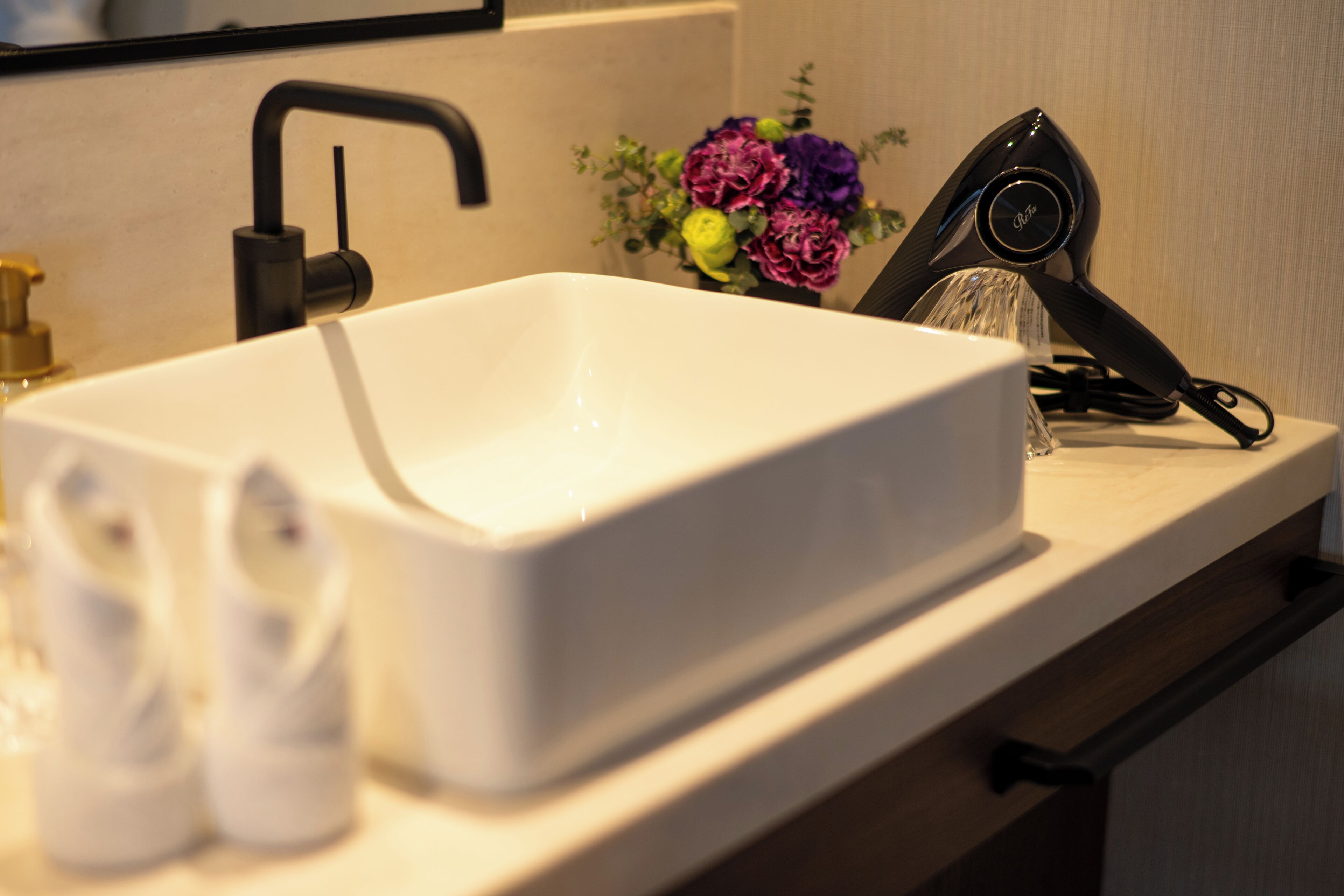 A white rectangular sink with a modern faucet, a small vase with flowers, and a hairdryer on the countertop.