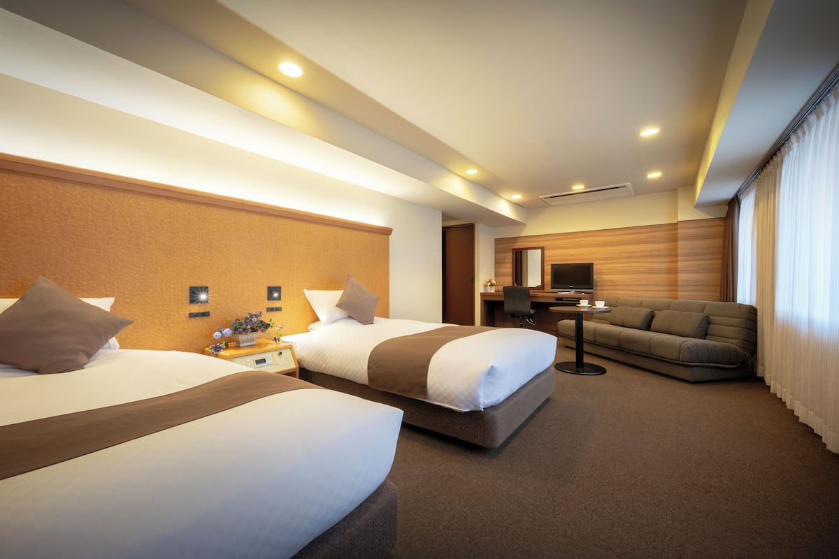 Ein Hotelzimmer mit zwei Betten, einem Schlafsofa, einem Schreibtisch und einem Fernseher.