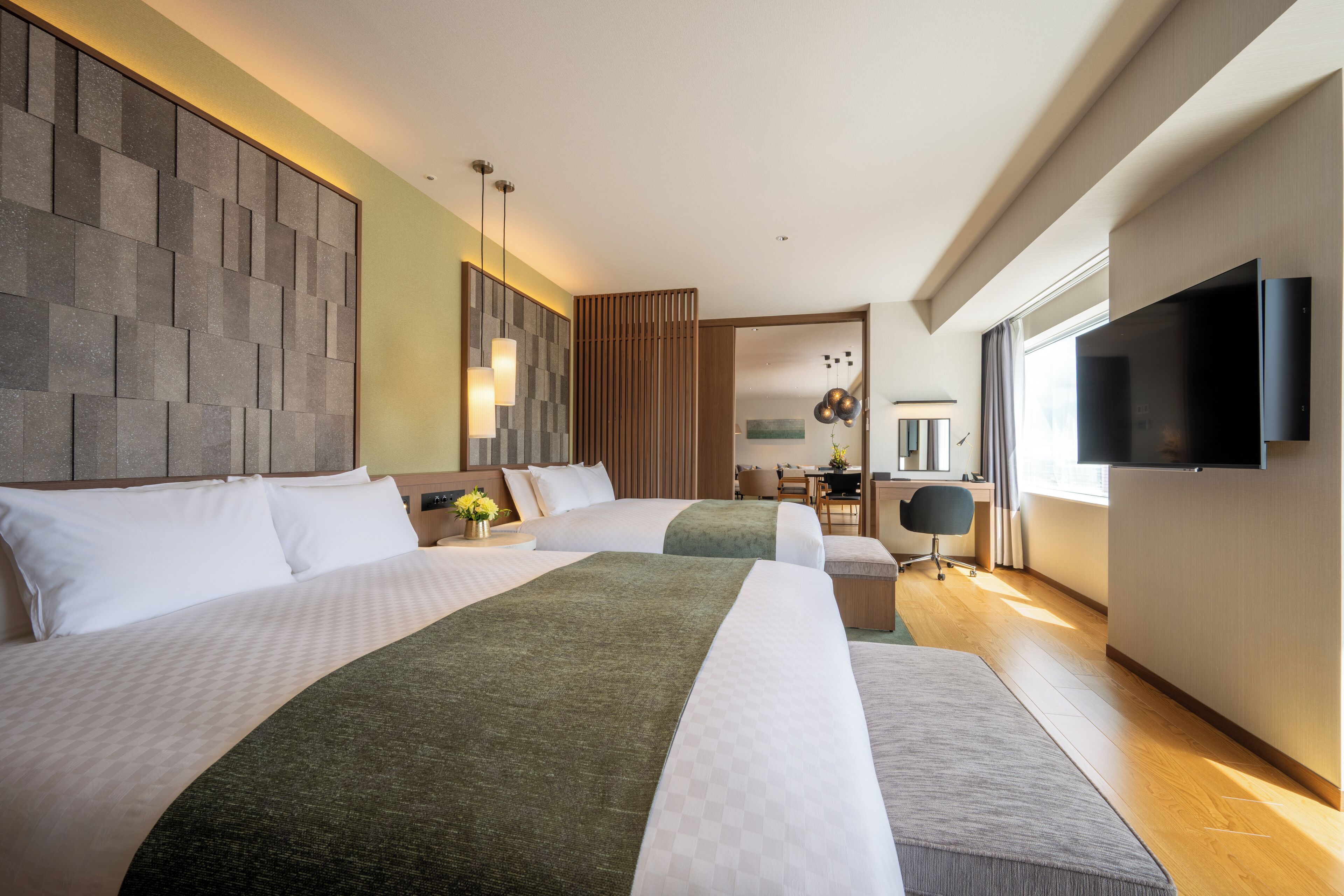 A hotel room with two beds, a desk, a chair, a TV, and a large window.