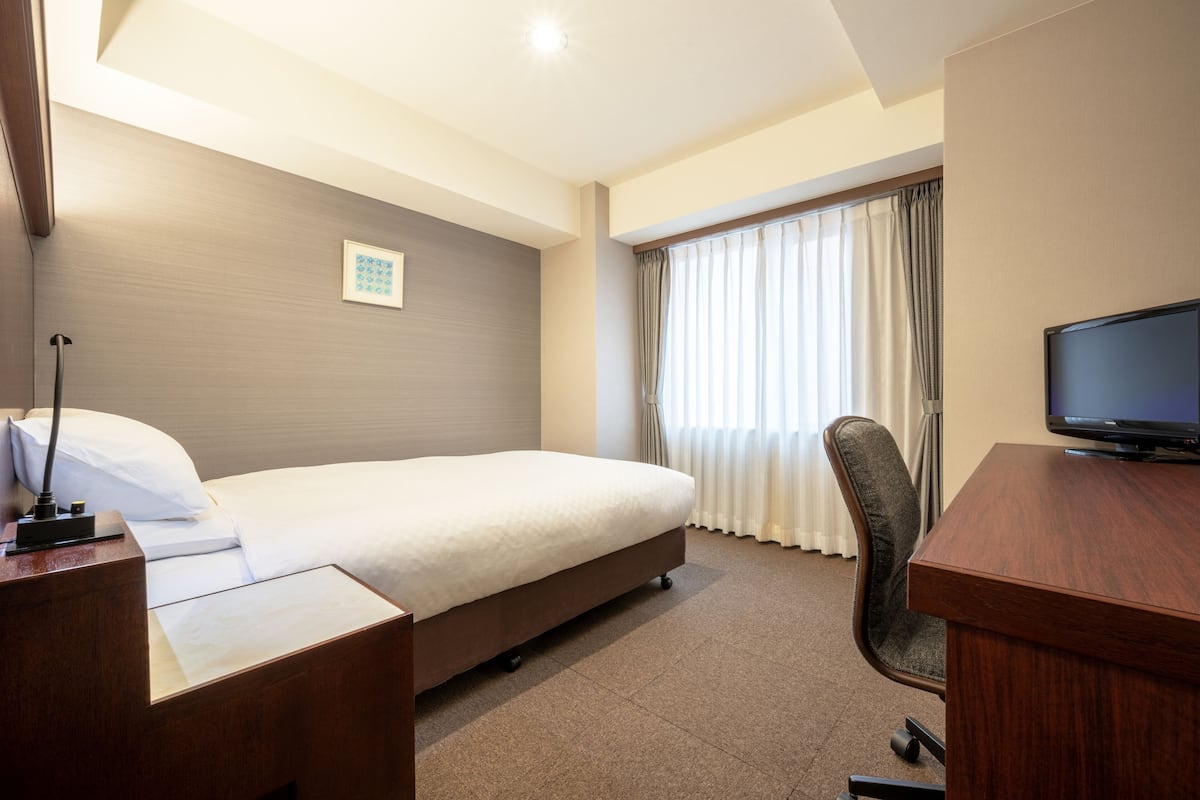 Ein Hotelzimmer mit Bett, Schreibtisch, Stuhl, Fernseher und Vorhängen.