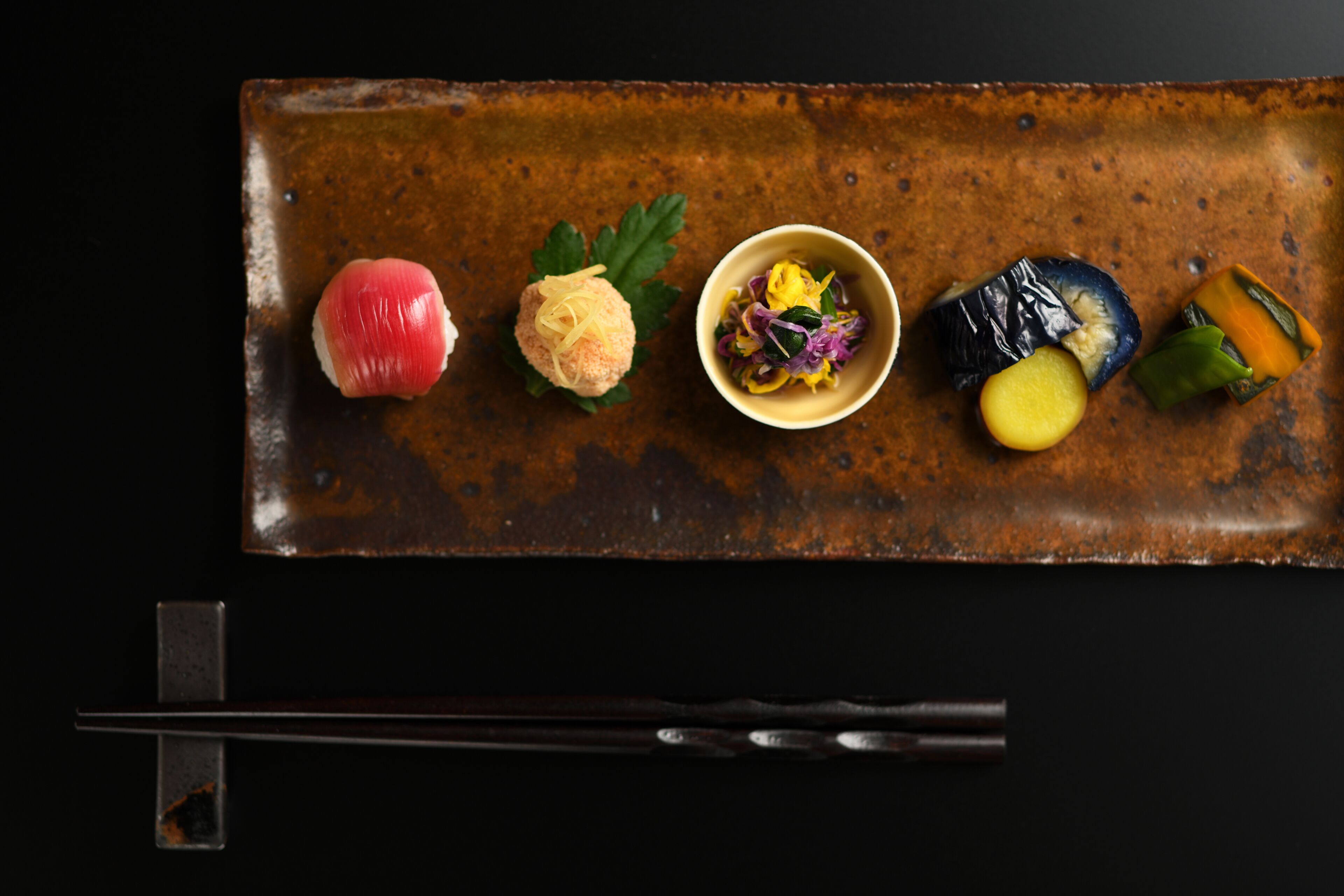 A rectangular metal tray with various food items and chopsticks.