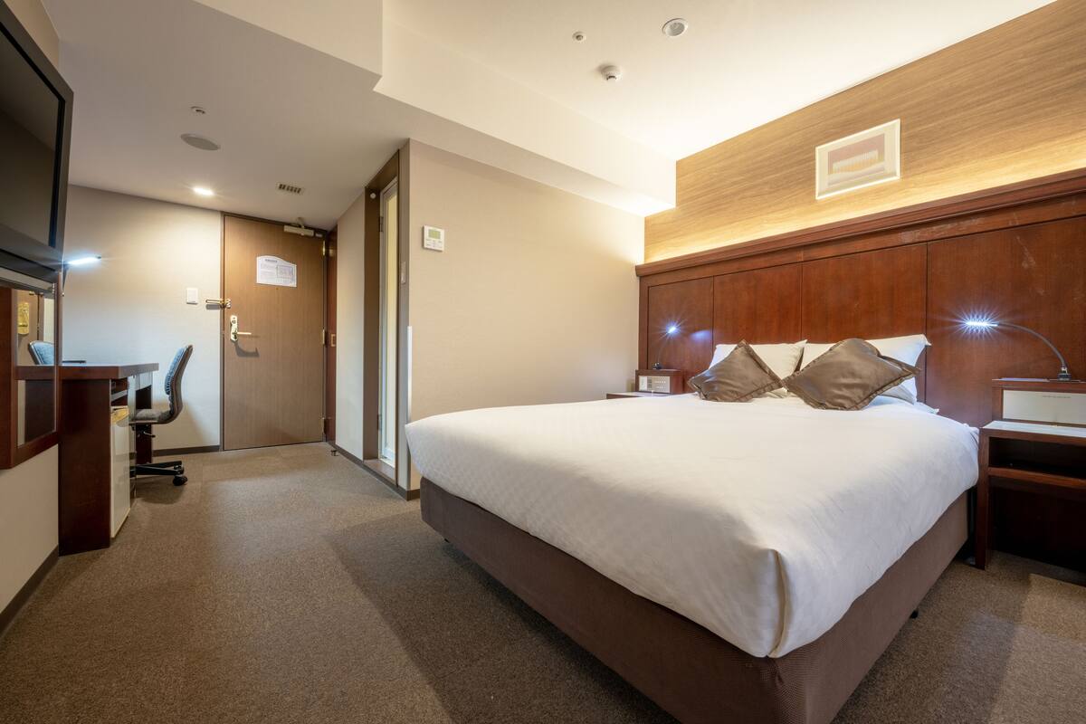 Ein Hotelzimmer mit einem großen Bett, einem Schreibtisch, einem Stuhl und einem hölzernen Kopfteil.