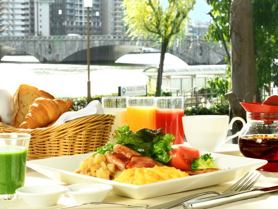 Una mesa de desayuno con cruasanes, huevos, tomates y jugo.