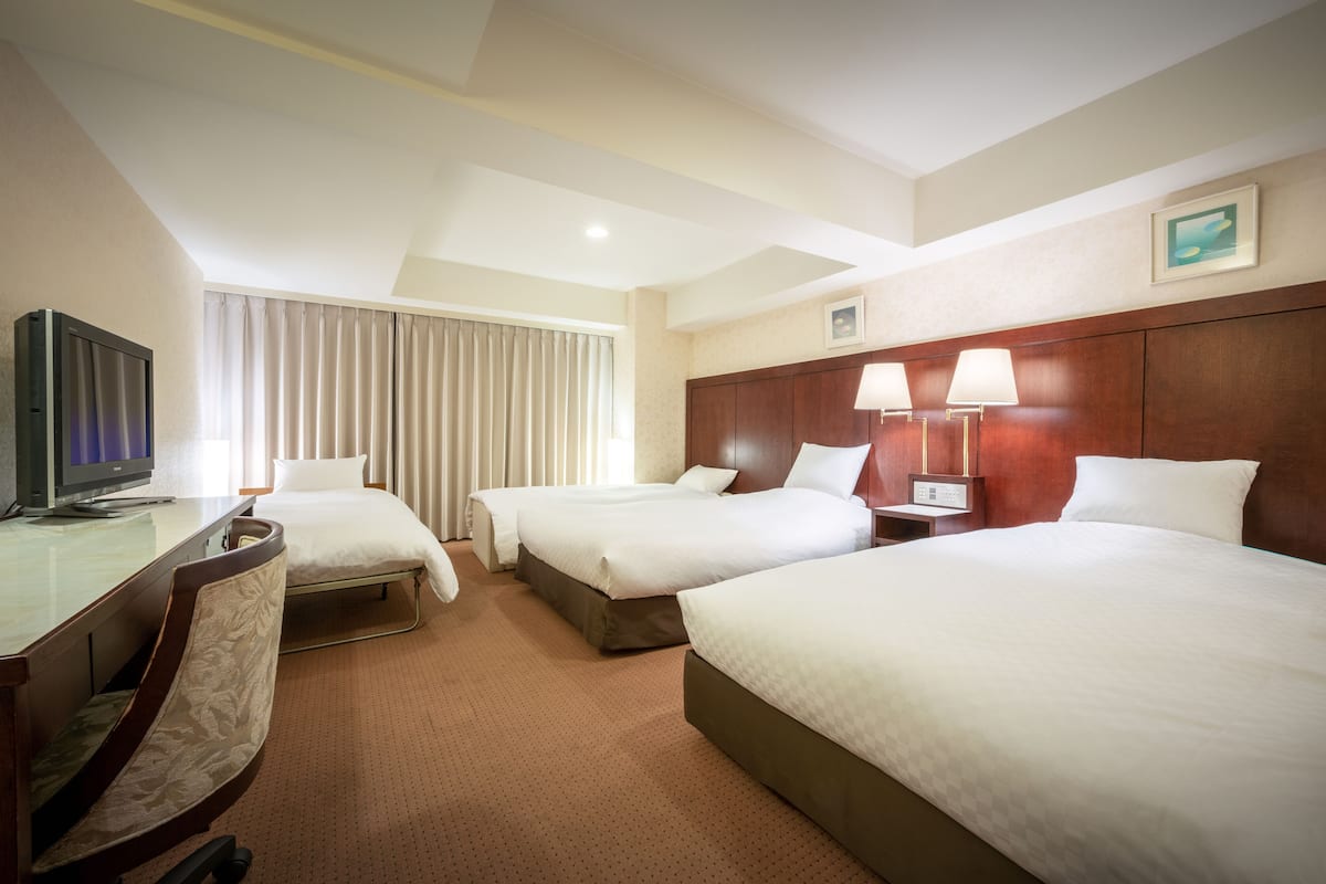 Ein Hotelzimmer mit zwei Betten, einem Schreibtisch mit Fernseher und einem Fenster mit Vorhängen.