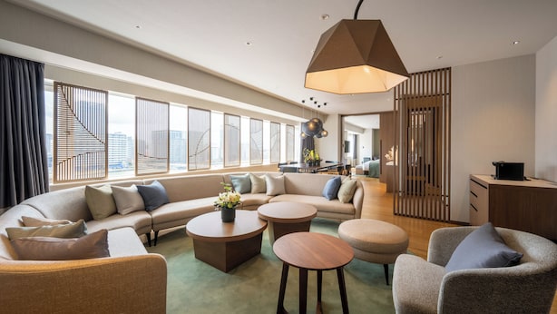 A modern hotel room with a large L-shaped sofa, two round coffee tables, and a seating area with a small round table. - Niigata Grand Hotel (Niigata)