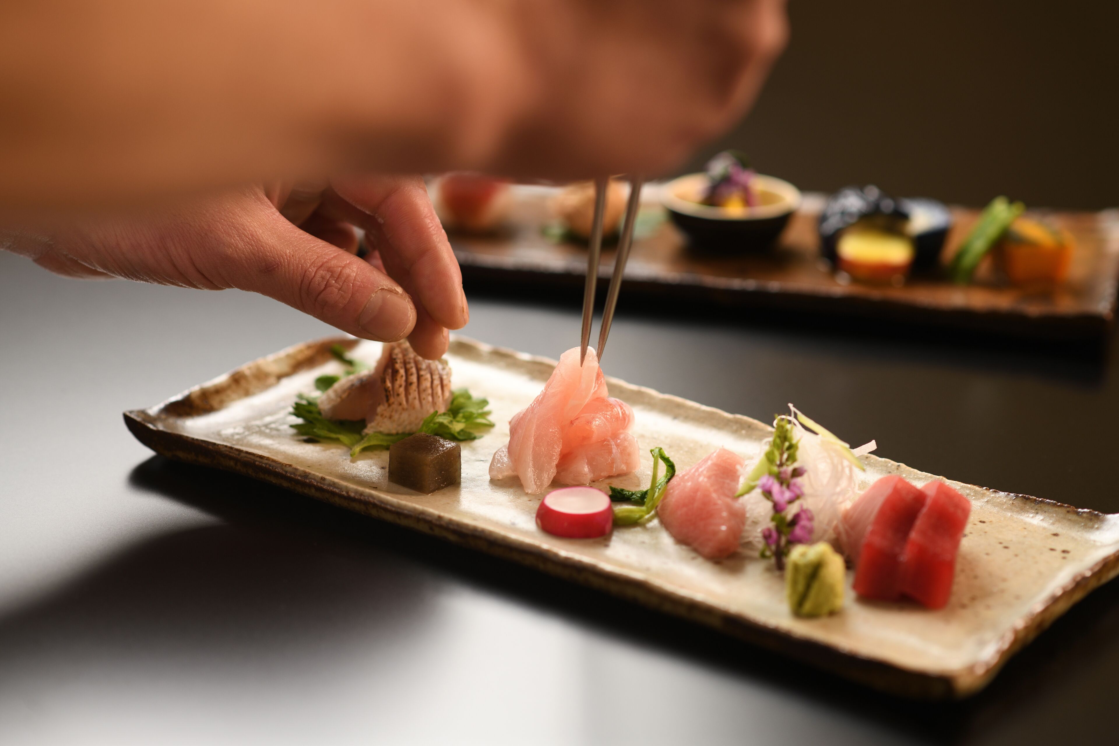 A hand using chopsticks to pick up a piece of sushi on a rectangular plate.