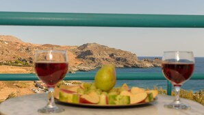 A table with a plate of fruit and two glasses of red wine, overlooking a coastal landscape with mountains and the sea. - Sokol Resort (Agios Vasileios)