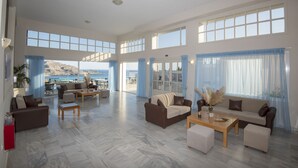 A spacious living area with multiple seating options, large windows, and a view of the sea. - Sokol Resort (Agios Vasileios)
