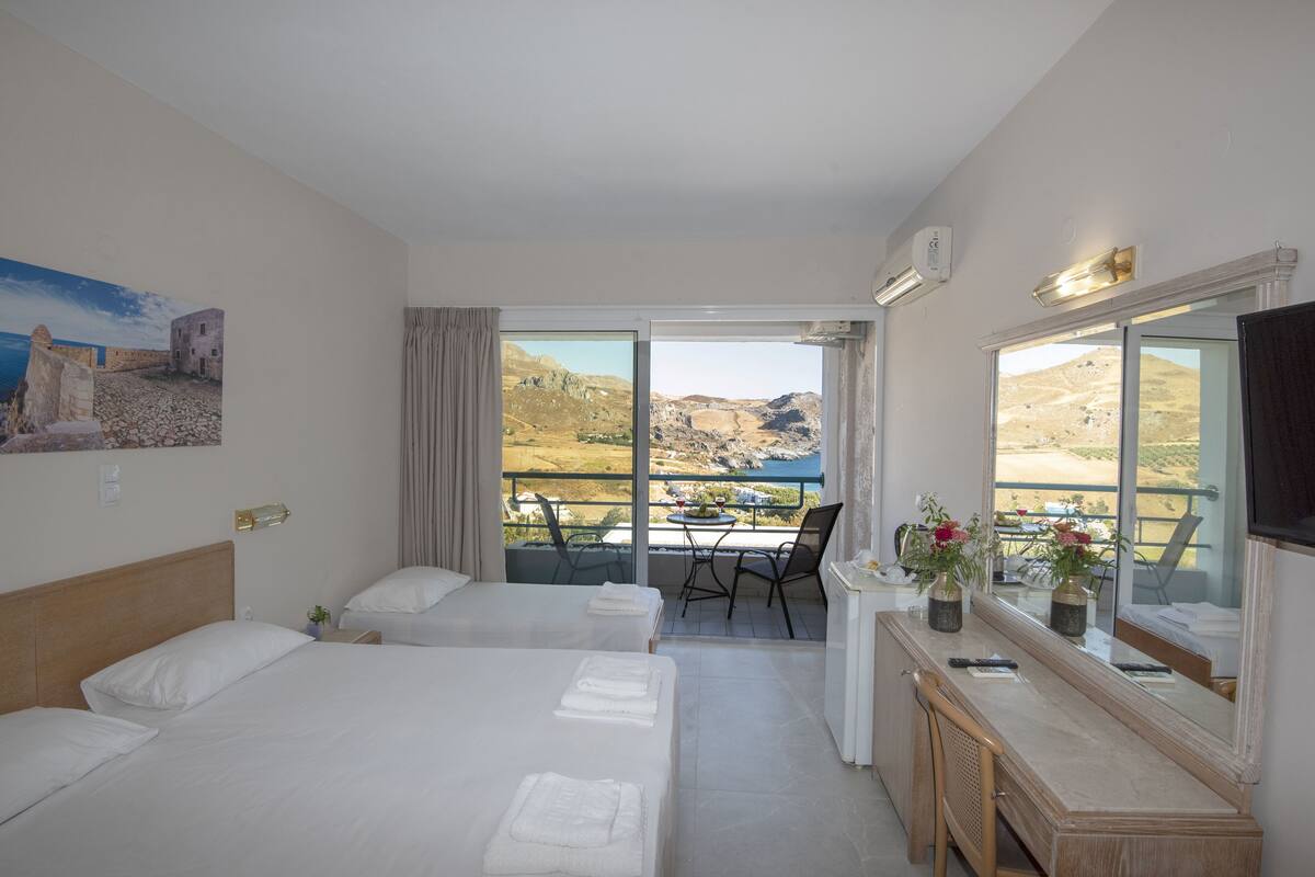 A hotel room with two beds, a balcony with a table and chairs, and a view of the landscape.