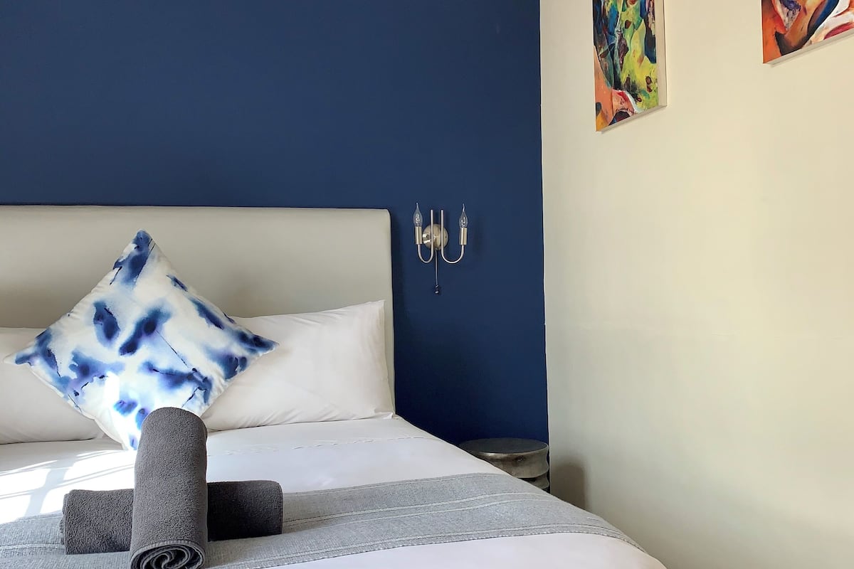 A neatly made bed with a white and gray bedspread, a blue and white pillow, and rolled towels.