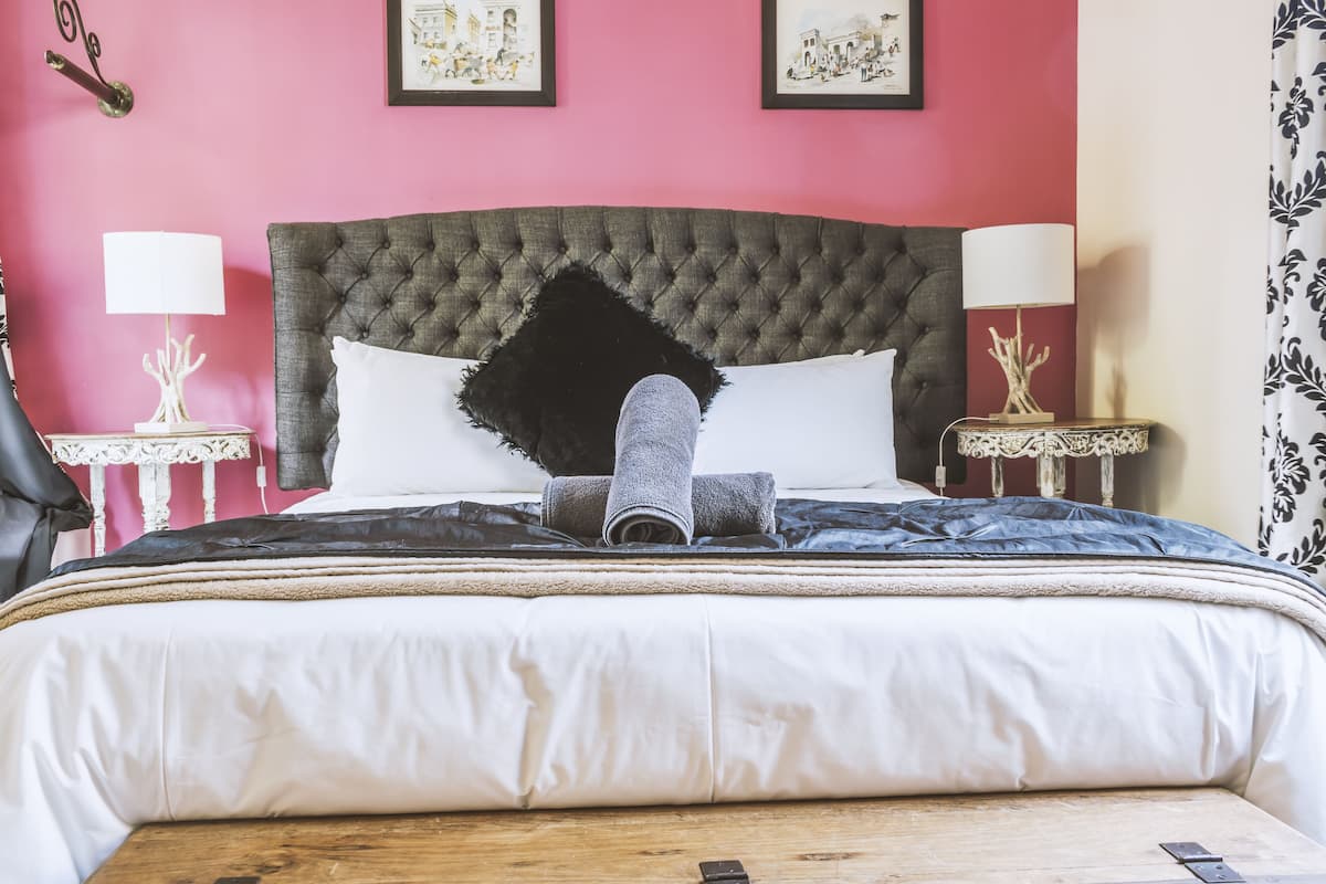 A neatly made bed with a grey headboard, white and black bedding, and a rolled towel. There are two bedside tables with lamps and framed pictures on the walls.