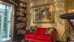 A cozy room with a red sofa, a bookshelf filled with books, and a framed painting on the wall. - La Rose B&B (Cape Town)