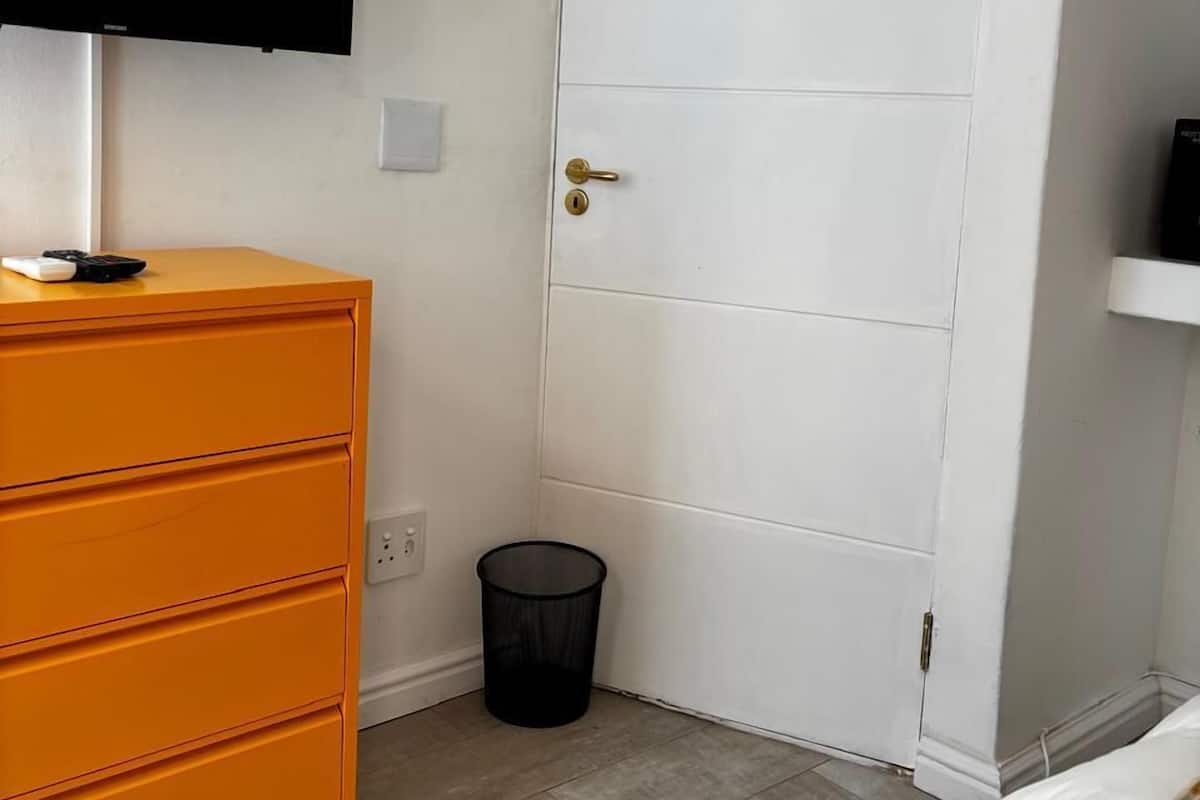 A room with a white door, a television mounted on the wall, and an orange dresser with drawers.