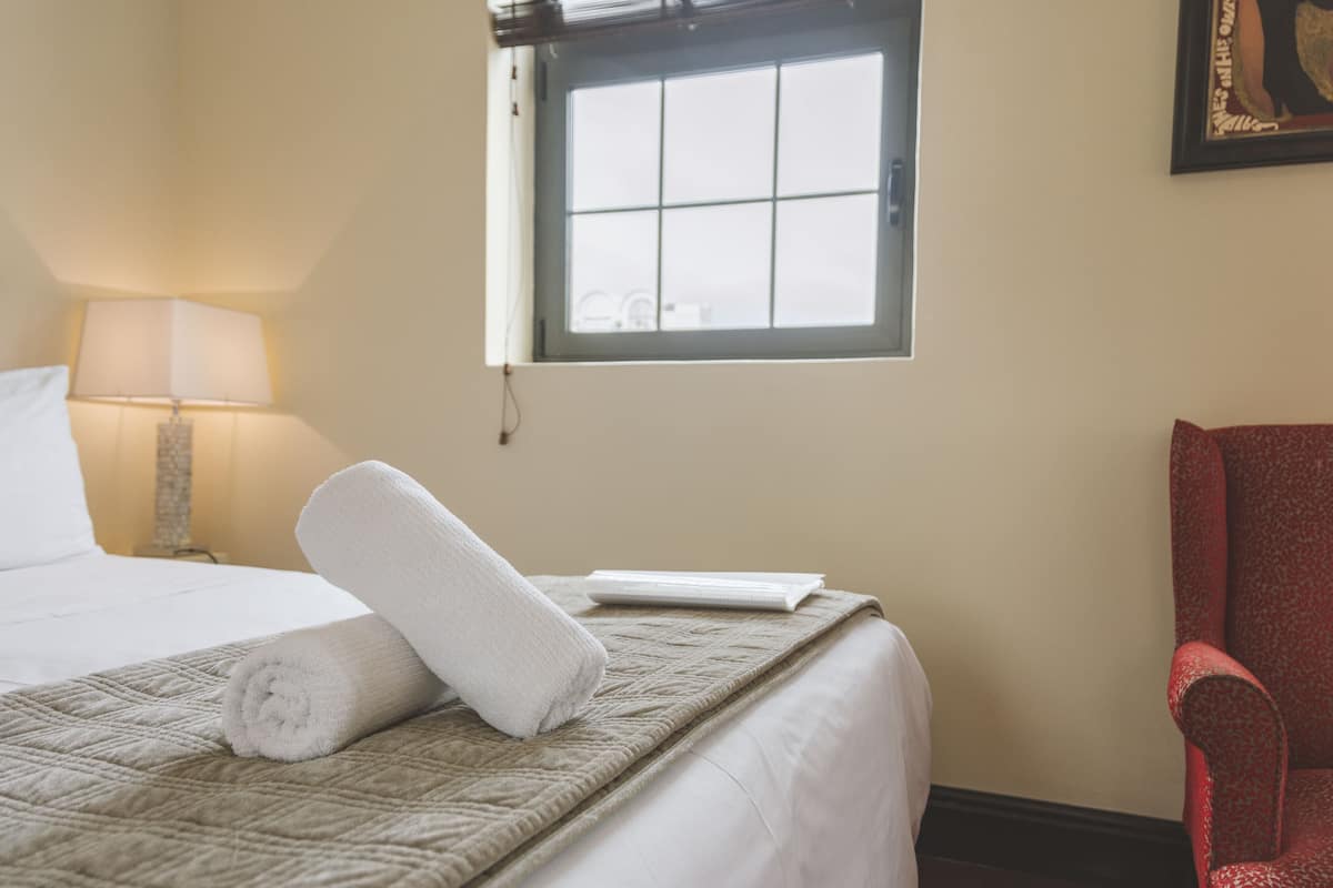 A hotel room with a bed, a window, a red chair, and a lamp.