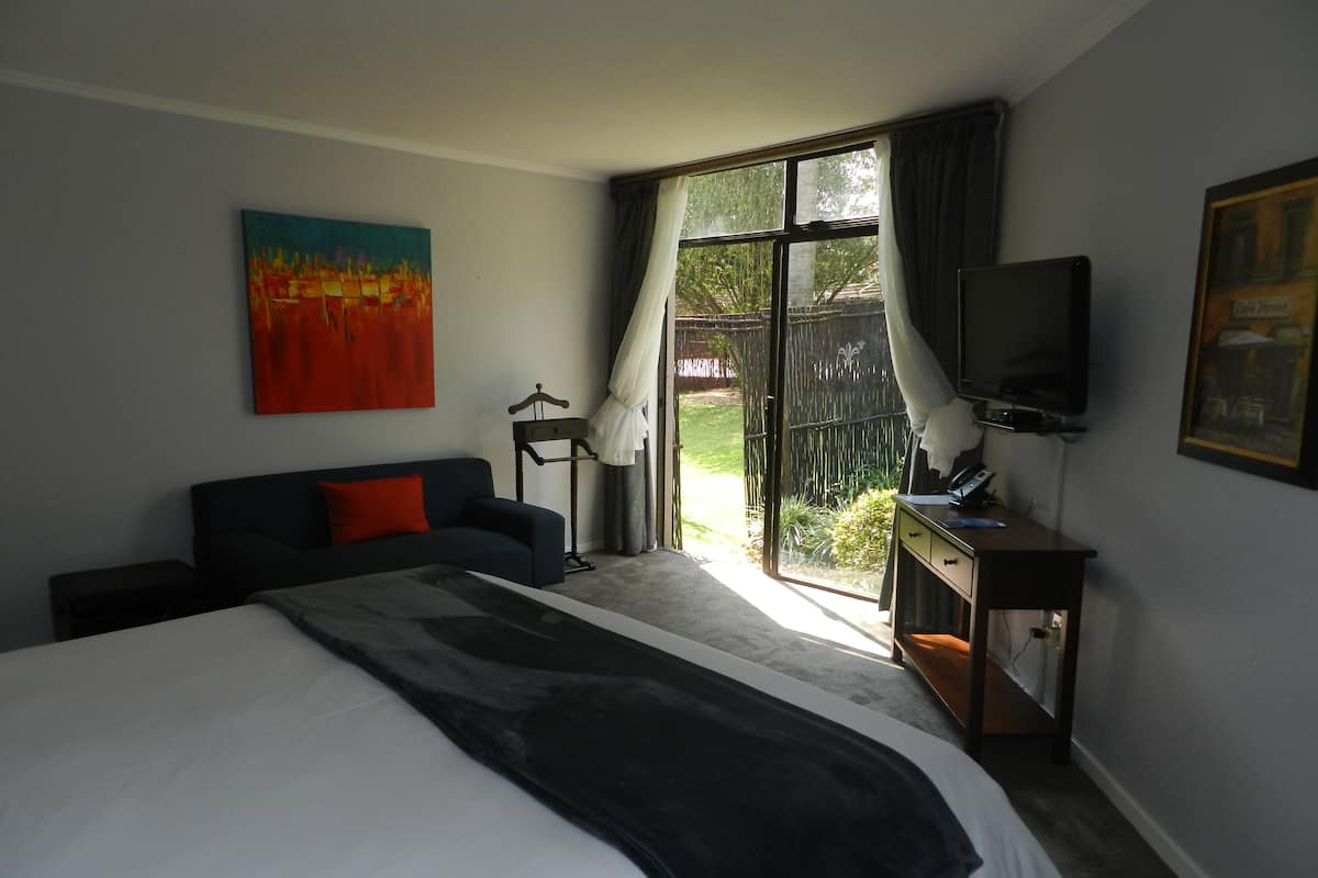 Quarto com uma cama grande, uma escrivaninha com computador, uma televisão e um quadro na parede.