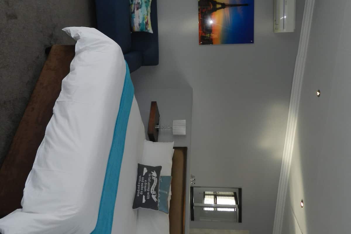 Um quarto com cama, um sofá azul, uma pintura de um pôr do sol e um aparelho de ar condicionado.