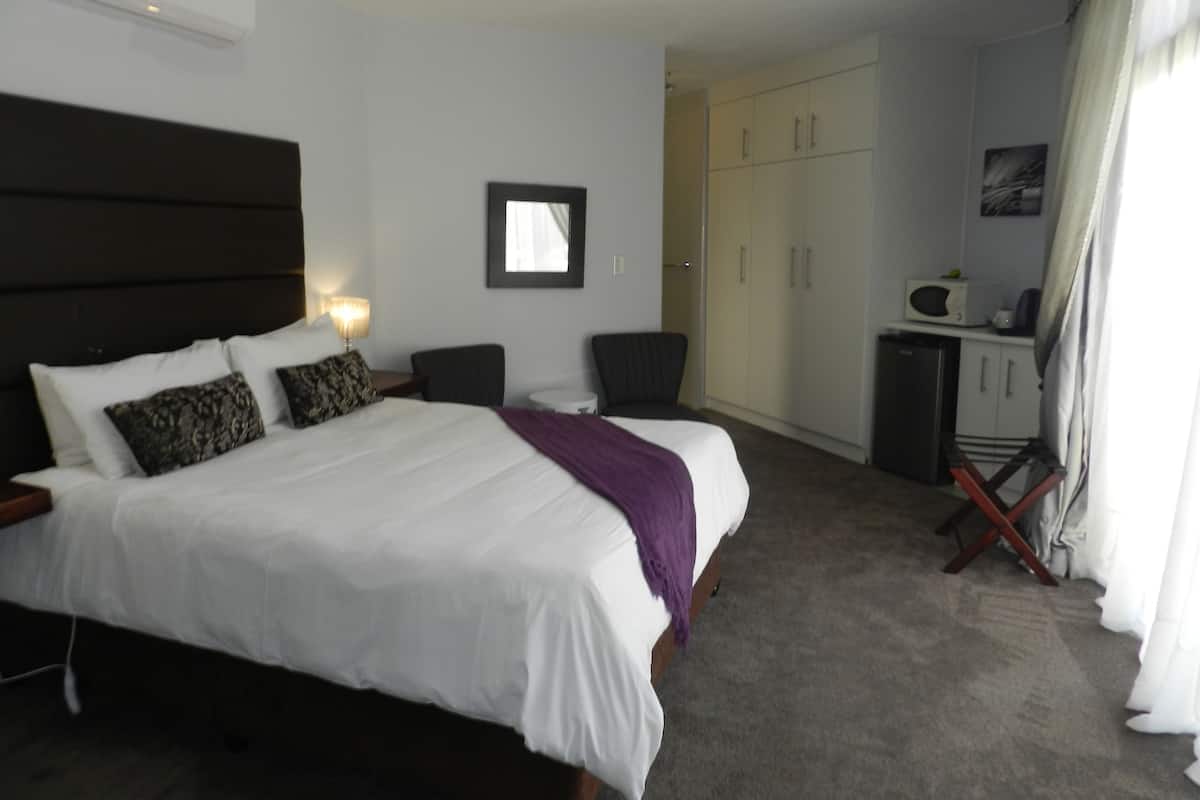 Quarto de hotel com uma cama grande, uma escrivaninha, uma cadeira, um guarda-roupa e um micro-ondas.