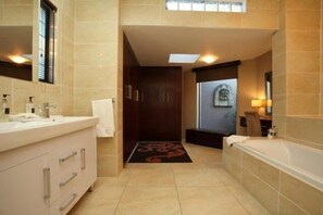 A modern bathroom with a large bathtub, a vanity with a mirror, and a shower area. - Le Petit Fillan (Sandton)