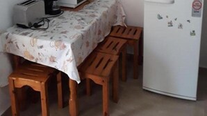 A small kitchenette with a microwave, toaster, and refrigerator. There is a table with a floral tablecloth and wooden chairs. - Christina Apts and Studios (Corfu)