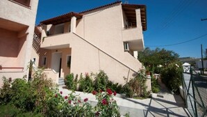 A two-story building with a sloped roof, a small balcony, and a garden with red flowers. - Christina Apts and Studios (Corfu)