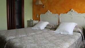 A double bed with a floral-patterned bedspread, two white pillows, and a nightstand with a lamp. - Goya Suites (Salamanca)
