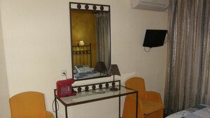 A hotel room with a glass desk, two chairs, a bed, a TV, and a mirror. - Goya Suites (Salamanca)
