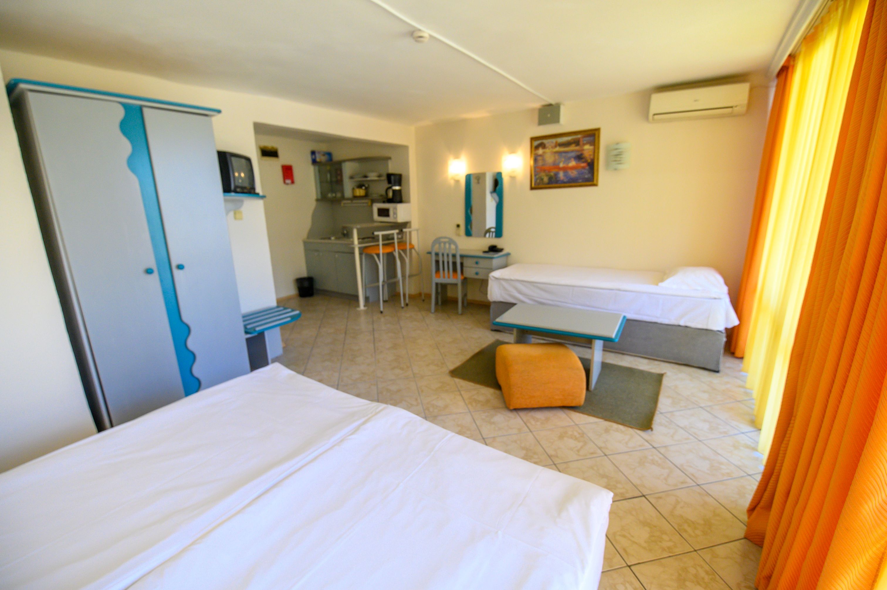 A hotel room with two beds, a kitchenette, a desk, and a chair.