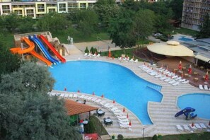 A swimming pool with a water slide, lounge chairs, and a covered area with tables and umbrellas. - Iskar (Nessebar)