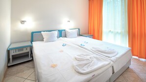 A hotel room with a bed, two bedside tables, a nightstand, and a window with orange curtains. - Iskar (Nessebar)