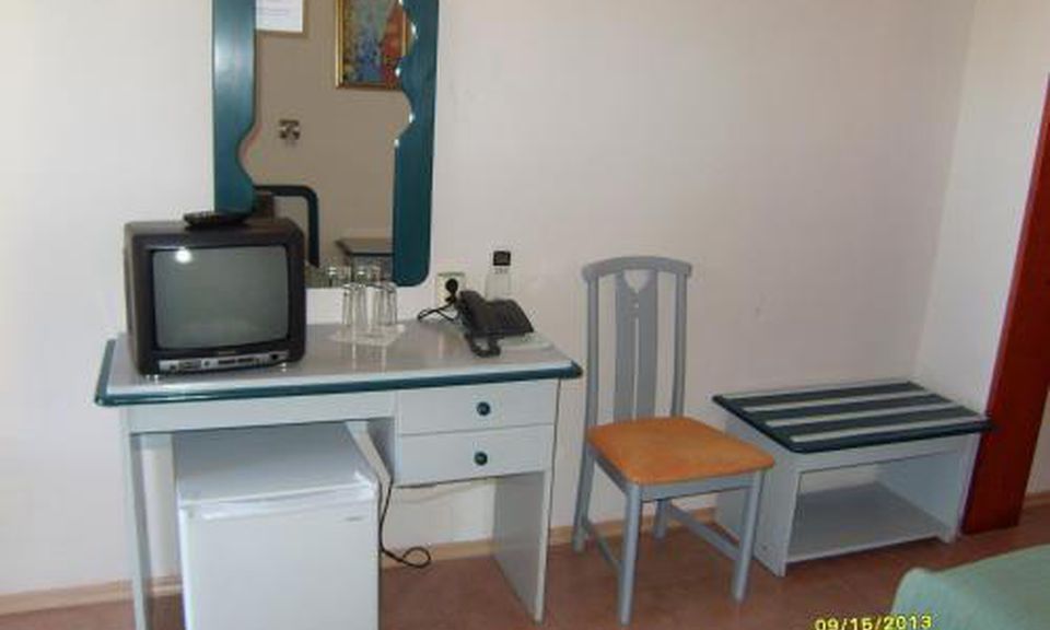 A small, compact room with a single bed, a desk with a television, a chair, and a small table.