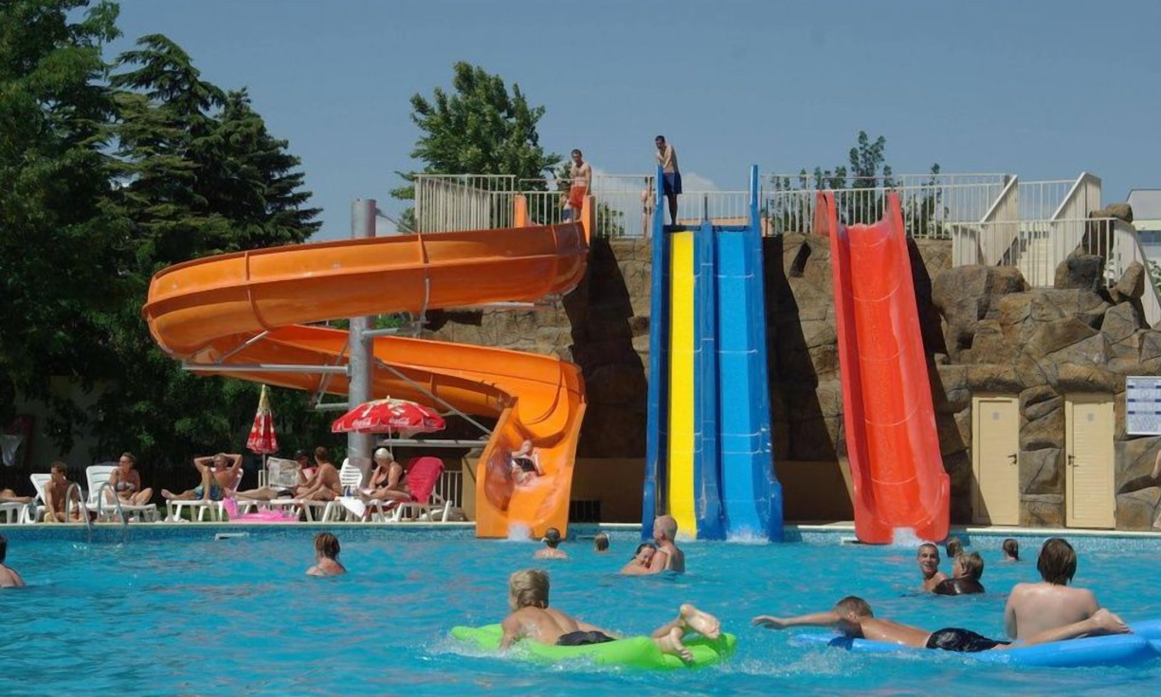 A swimming pool with multiple water slides and people swimming and playing.