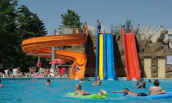 A swimming pool with multiple water slides and people swimming and playing.