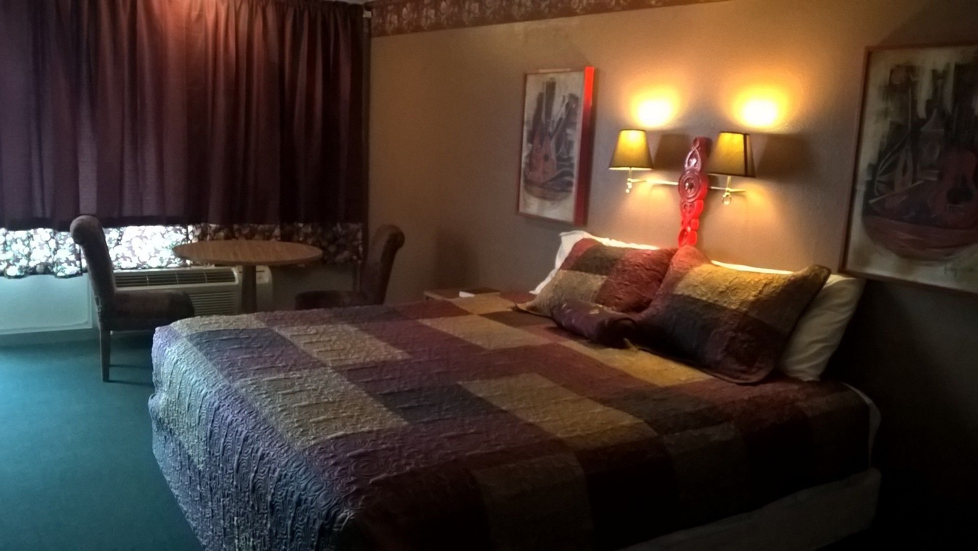 A hotel room with a bed, a chair, a small table, and two wall-mounted lamps.