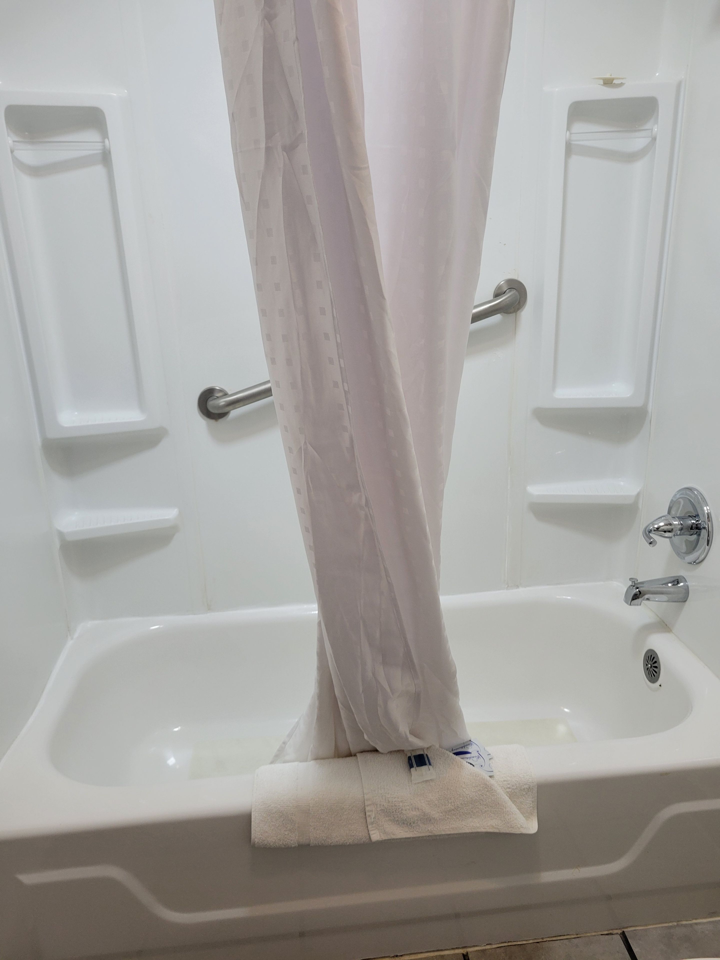A white bathtub with a shower curtain, a towel, and a handheld showerhead.
