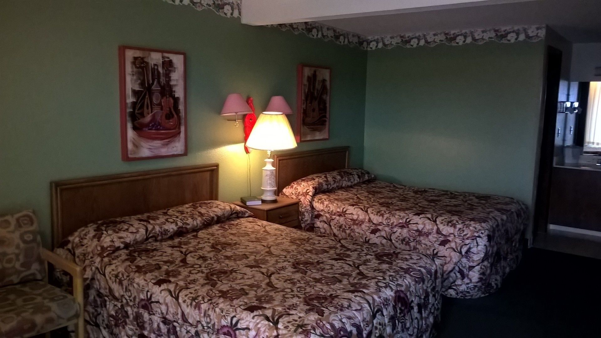 Una habitación de hotel con dos camas individuales, una mesita de noche con lámpara y dos cuadros colgados en la pared.