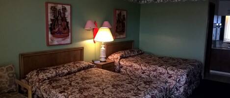 Una habitación de hotel con dos camas individuales, una mesita de noche con lámpara y dos cuadros colgados en la pared.