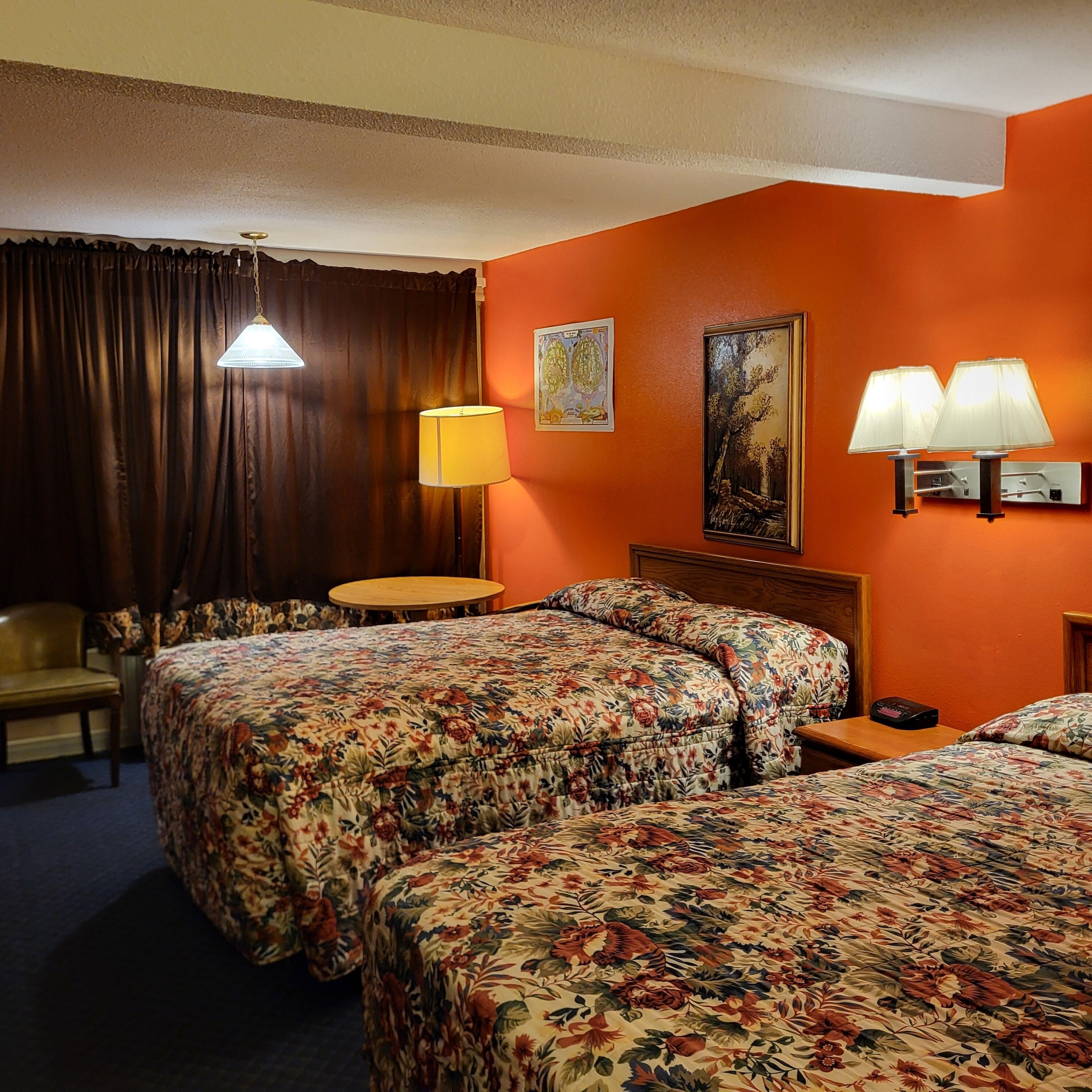 A hotel room with two beds, a desk, a chair, and a lamp.
