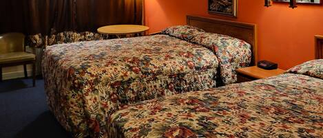 A hotel room with two beds, a desk, a chair, and a lamp.
