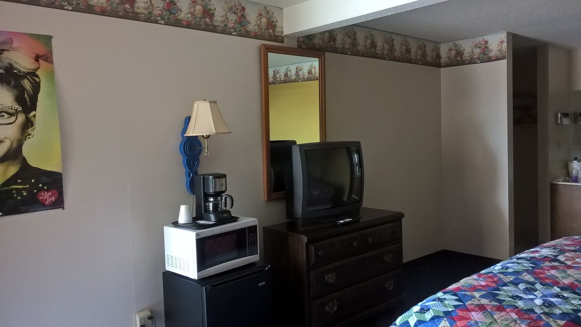 A hotel room with a bed, a dresser, a microwave, a coffee maker, a television, and a mirror.