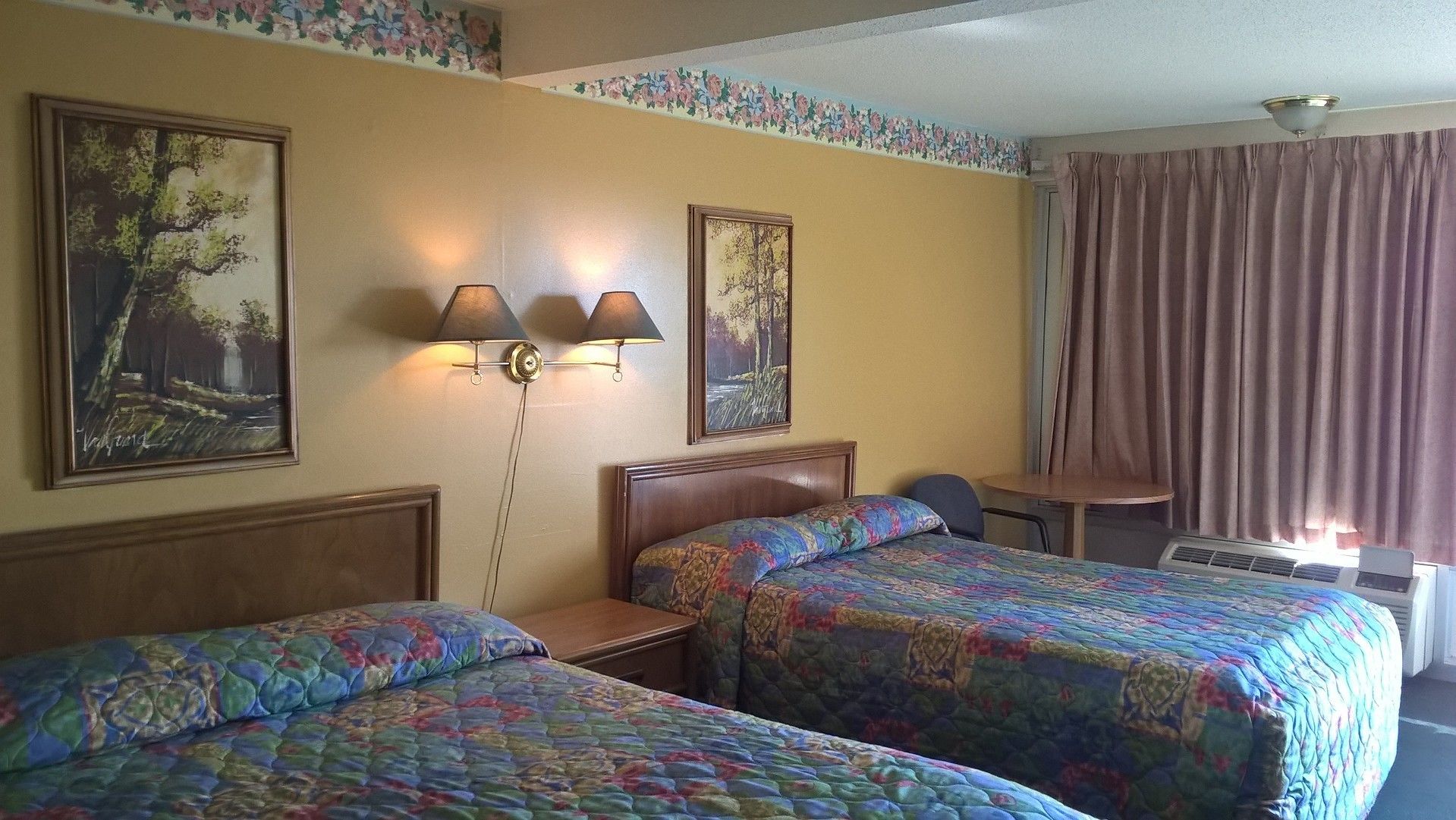 Ein Hotelzimmer mit zwei Betten, einem Schreibtisch, einem Stuhl, einer Lampe und einem Fenster mit Vorhängen.