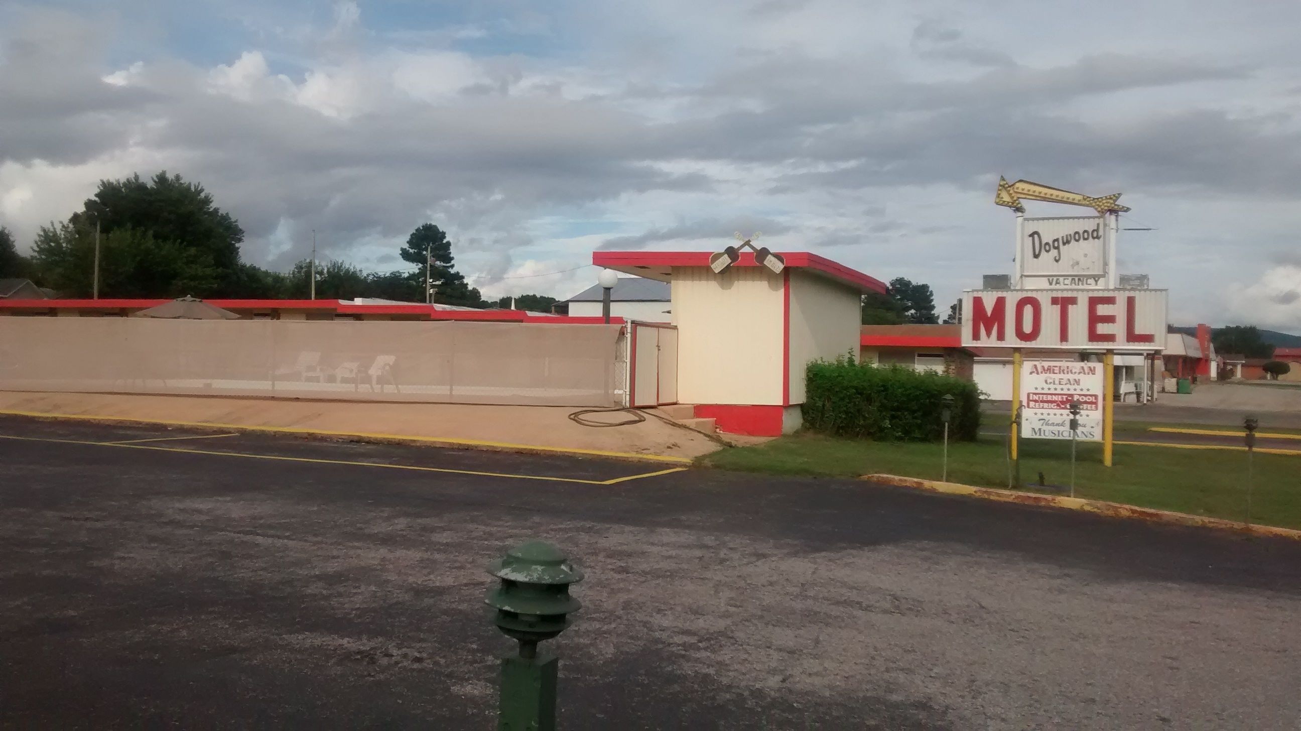 Un motel con un letrero rojo y blanco, un estacionamiento y una zona verde.