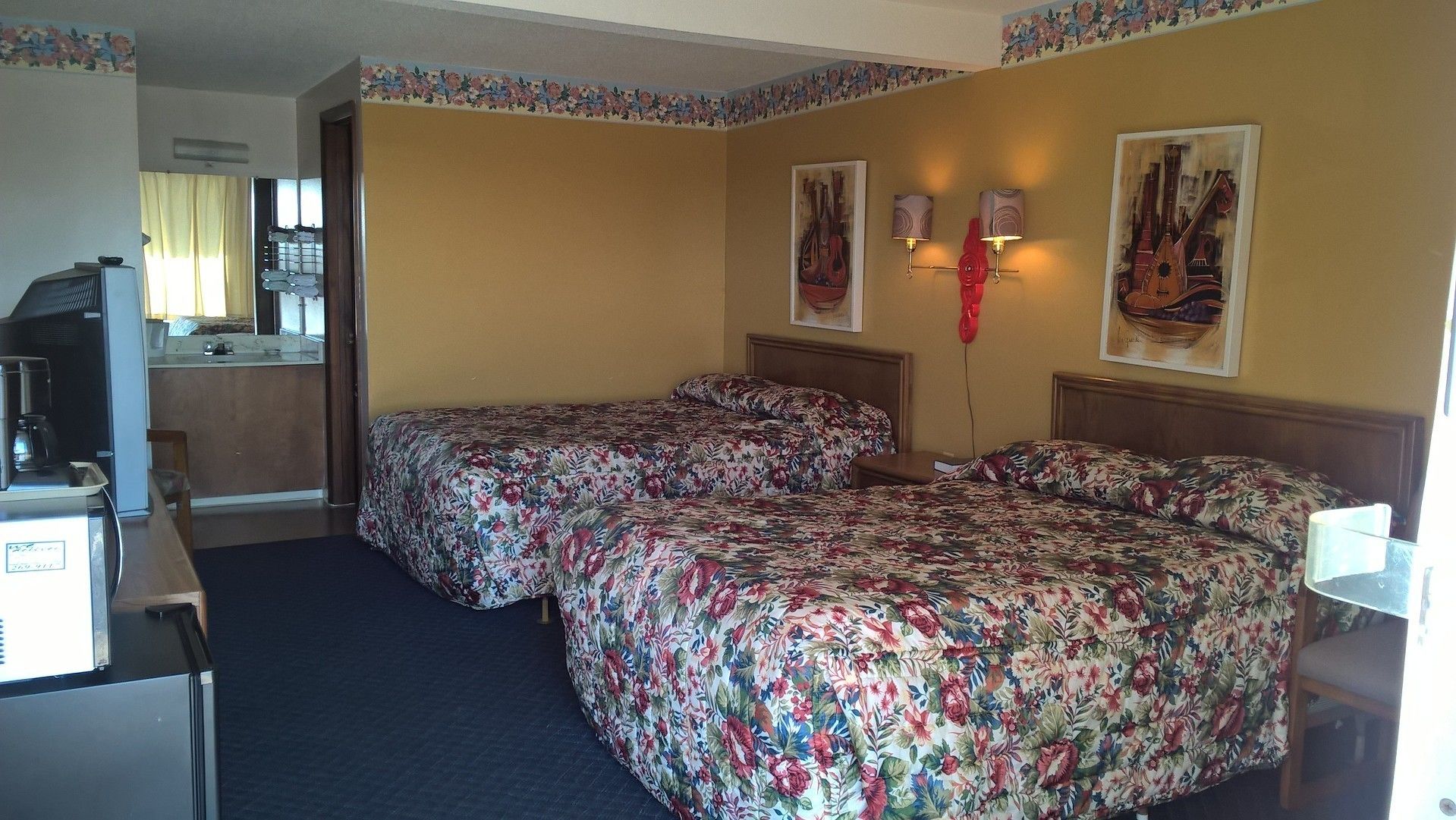 A hotel room with two beds, a kitchenette, and a dining area.
