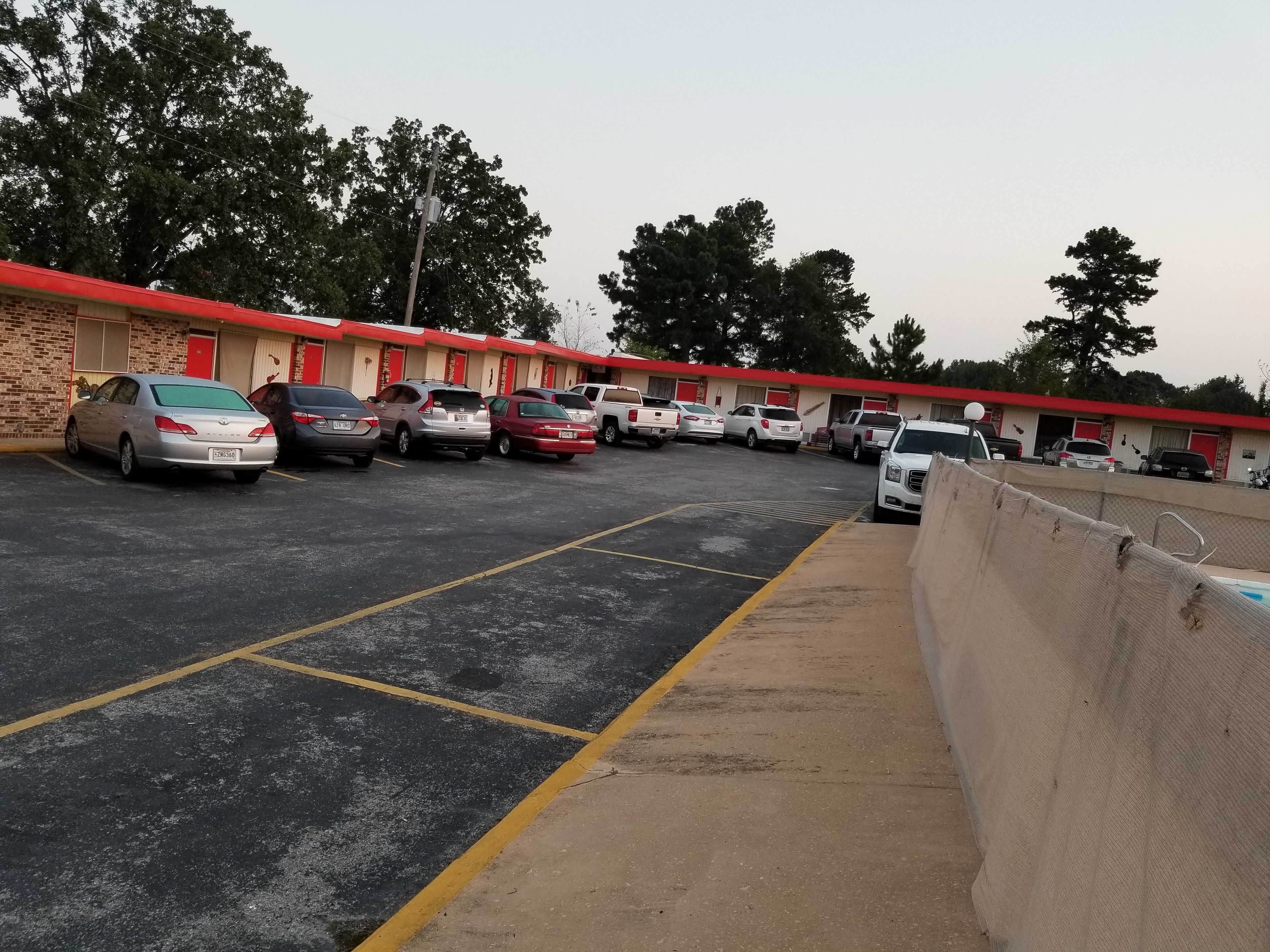 A parking lot with several cars parked in front of a motel with a red roof and brick walls.
