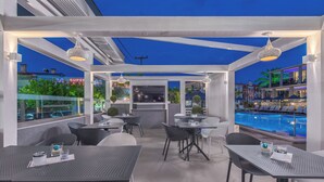 An outdoor patio area with tables and chairs, a pool, and a view of the city skyline. - Dionysos Hotel and Studios (Kassandra)