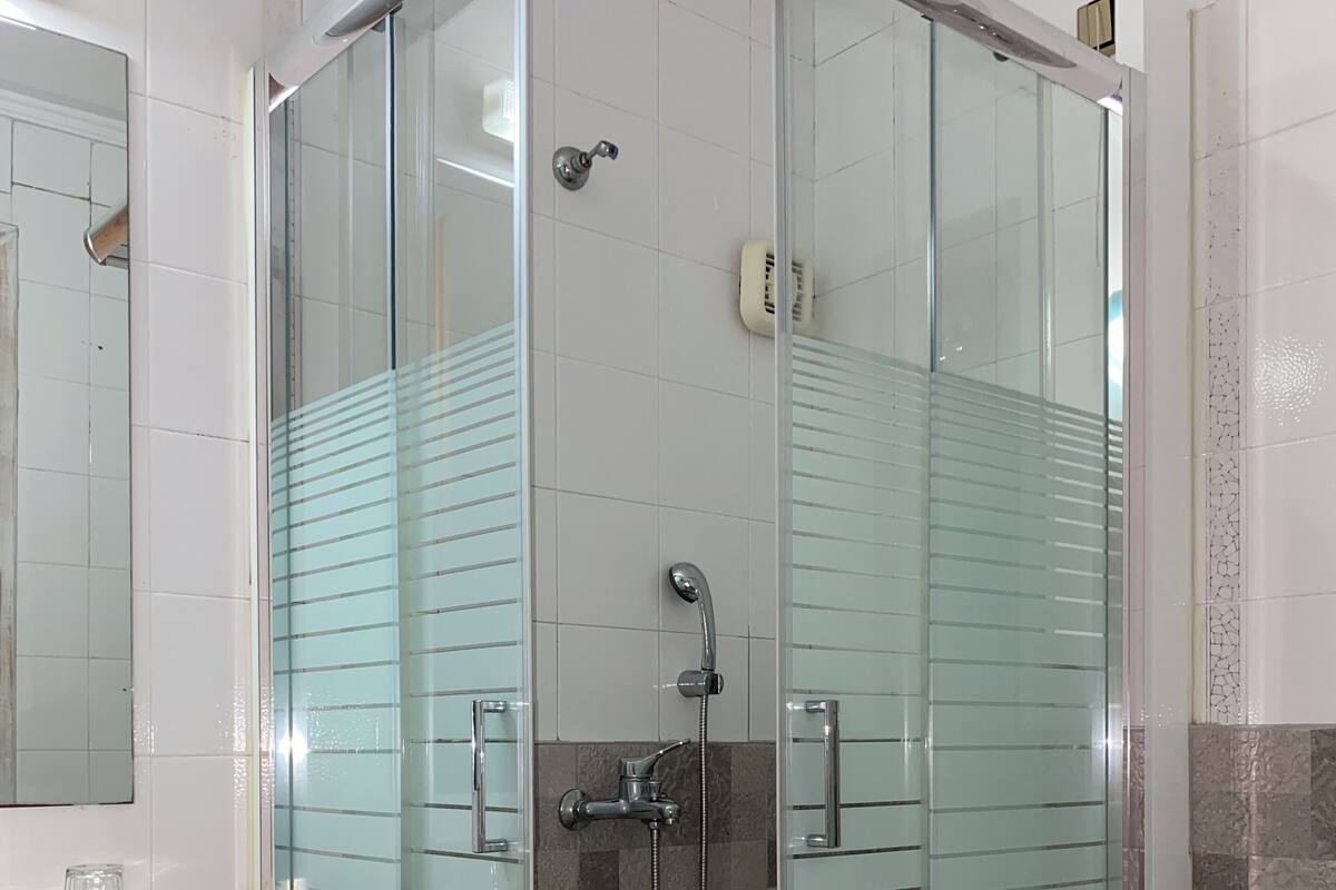 A glass-enclosed shower stall with a handheld showerhead, a sink with a wooden countertop, and a toilet.