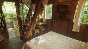 Une cabane en bois comprenant un lit, un escalier et un petit coin salon avec des chaises.